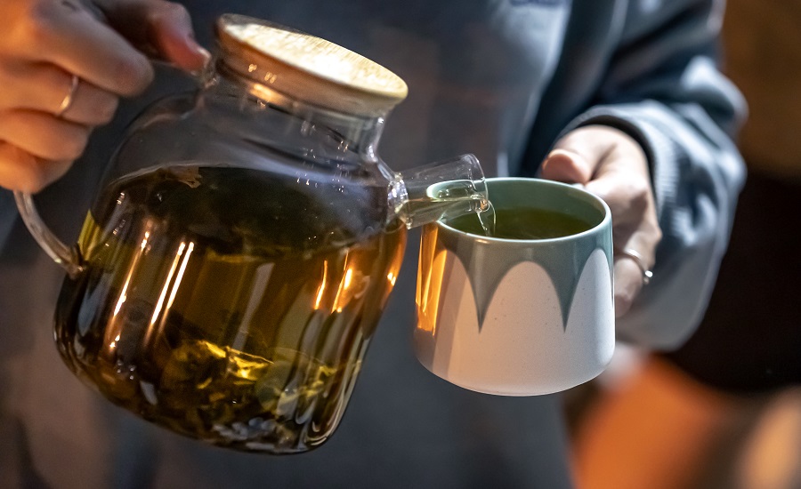 A woman pours tea into a cup late at night.
